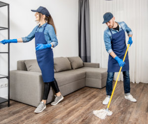 Two workers in blue overalls are cleaning a room